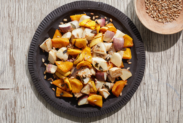 A picture of Roasted Turnips and Winter Squash With Agave Glaze from directly above. The orange and pale root vegetables sit on a slate grey plate with a brown bowl full of a darker brown grain sit in the upper right hand corner of the image.